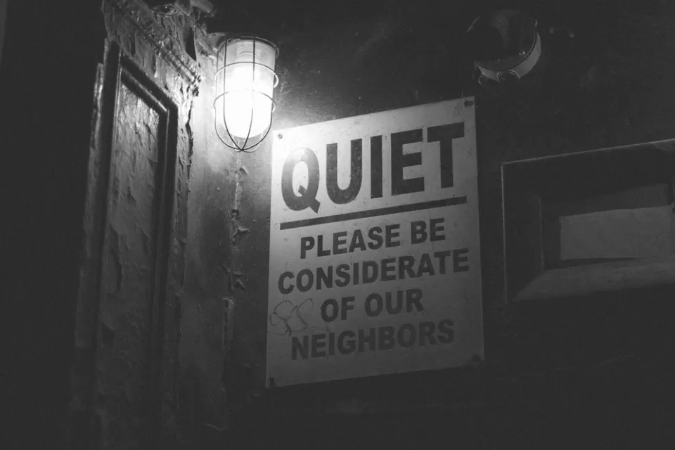 "QUIET Please be considerate of our neighbors" sign on outside of building with dim light